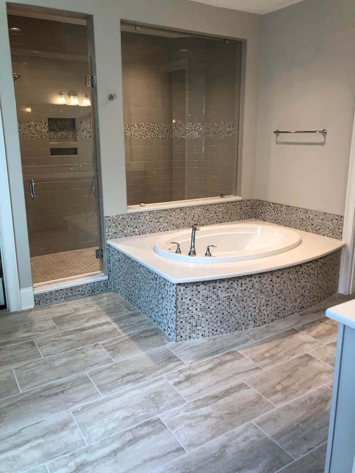 Bathroom with a white tub, shower with glass doors, and light gray tiled floors and walls.