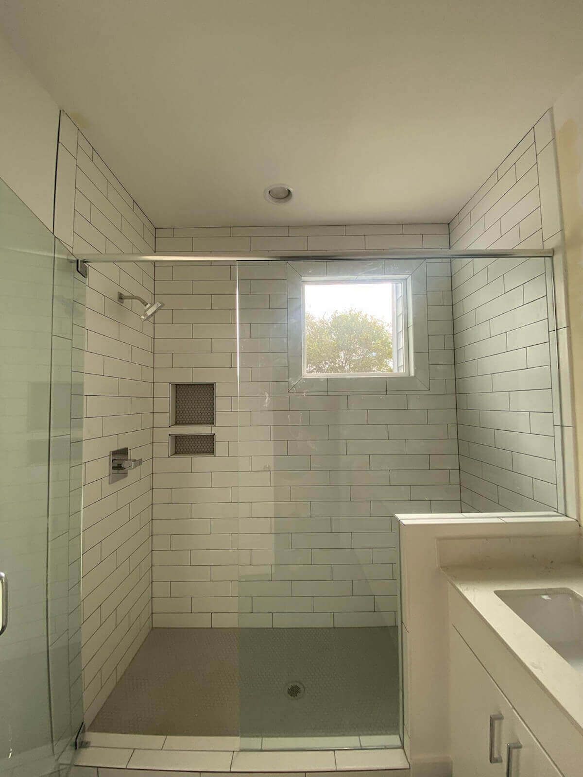 White tiled shower with glass door and small window.