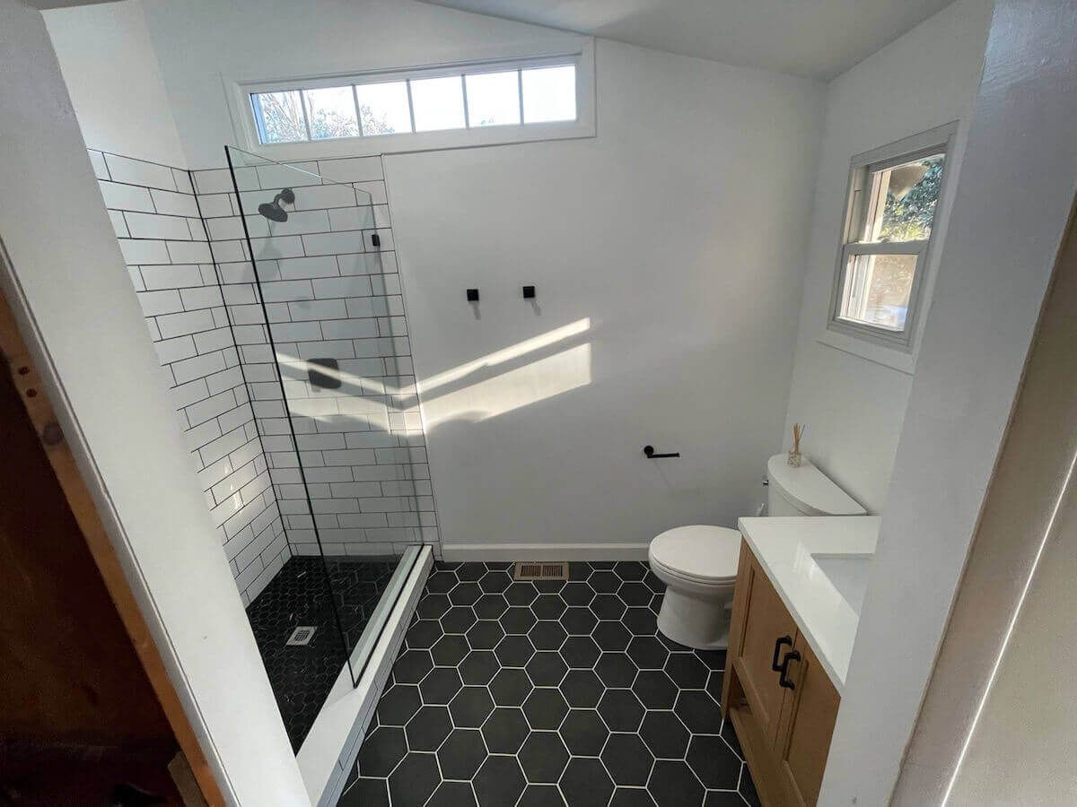 Bathroom with hexagonal black tile floor, white walls, glass shower, and wooden vanity.
