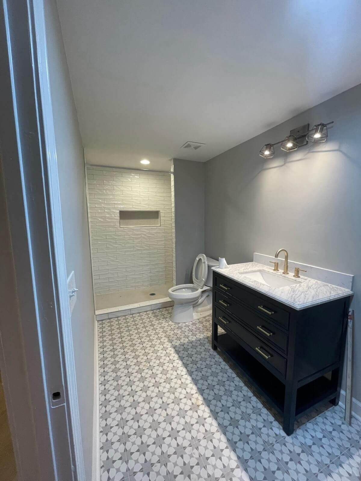 Bathroom with grey walls, patterned floor, shower, dark blue vanity, and toilet.