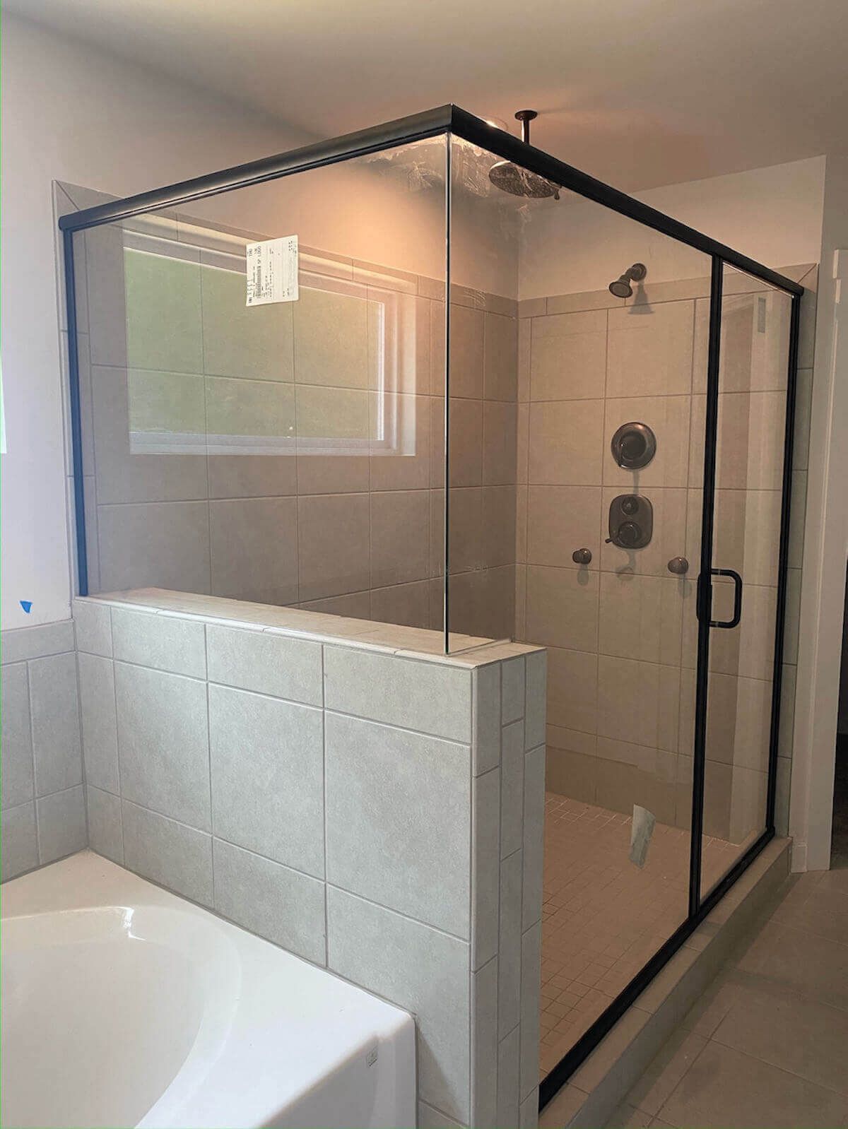 Shower stall with black frame and clear glass panels, light gray tiles.