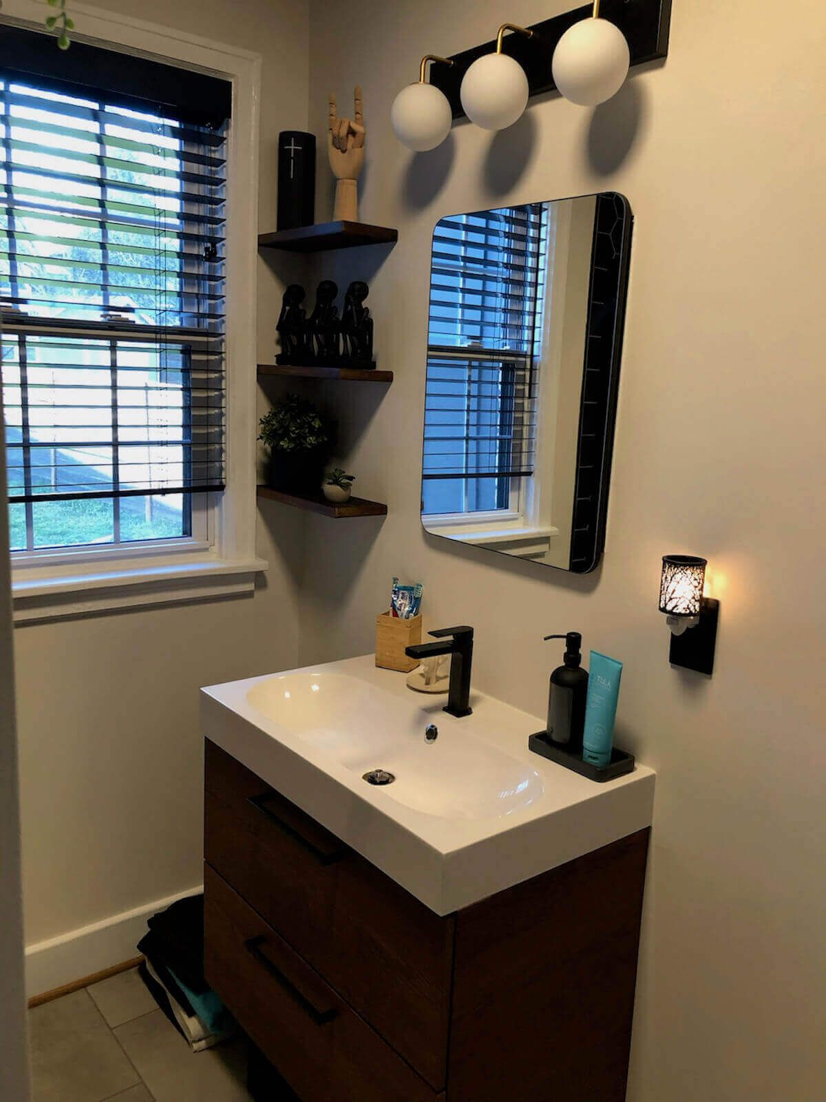 Modern bathroom with wooden vanity, white sink, black faucet, and three globe lights above the mirror.