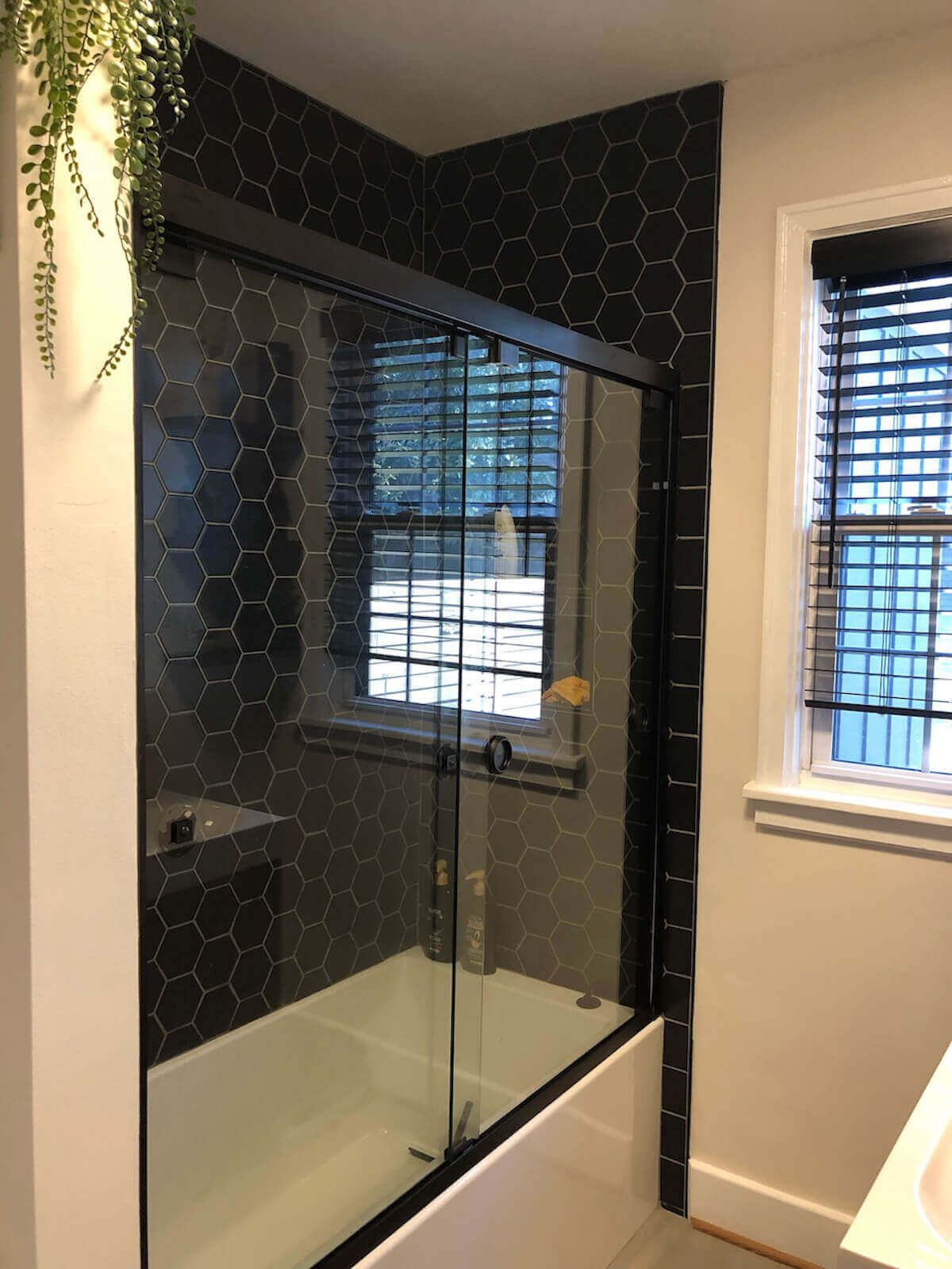 Black tiled shower with glass door, black frame, and a window.