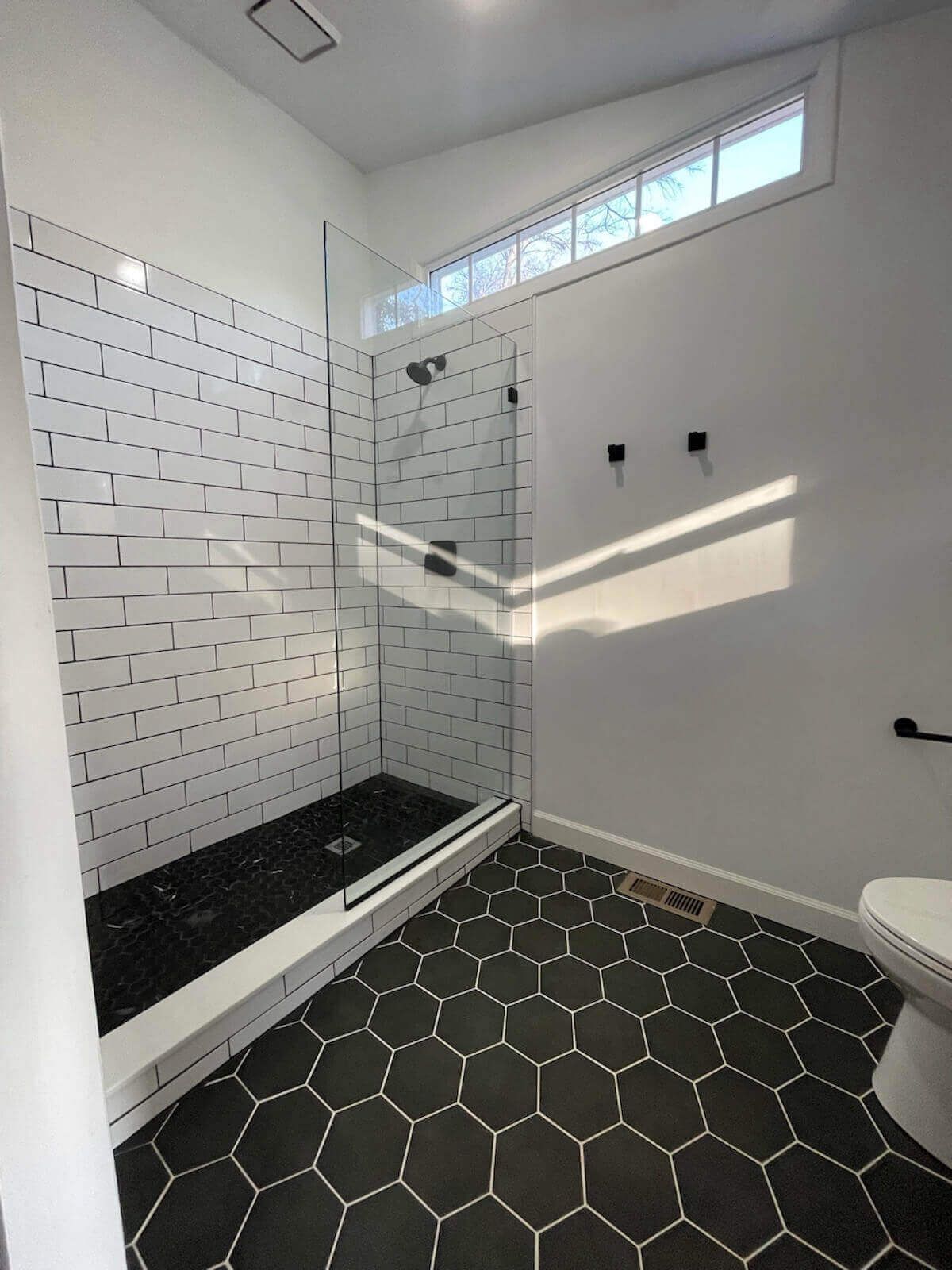 Bathroom with black hexagon floor tiles, subway tile shower walls, and a glass shower door.
