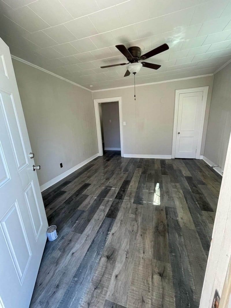Empty room with gray wood floors, light gray walls, and white doors and trim. A ceiling fan is visible.