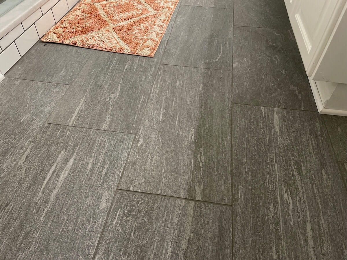 Gray stone tile floor with a small patterned rug in a bathroom.