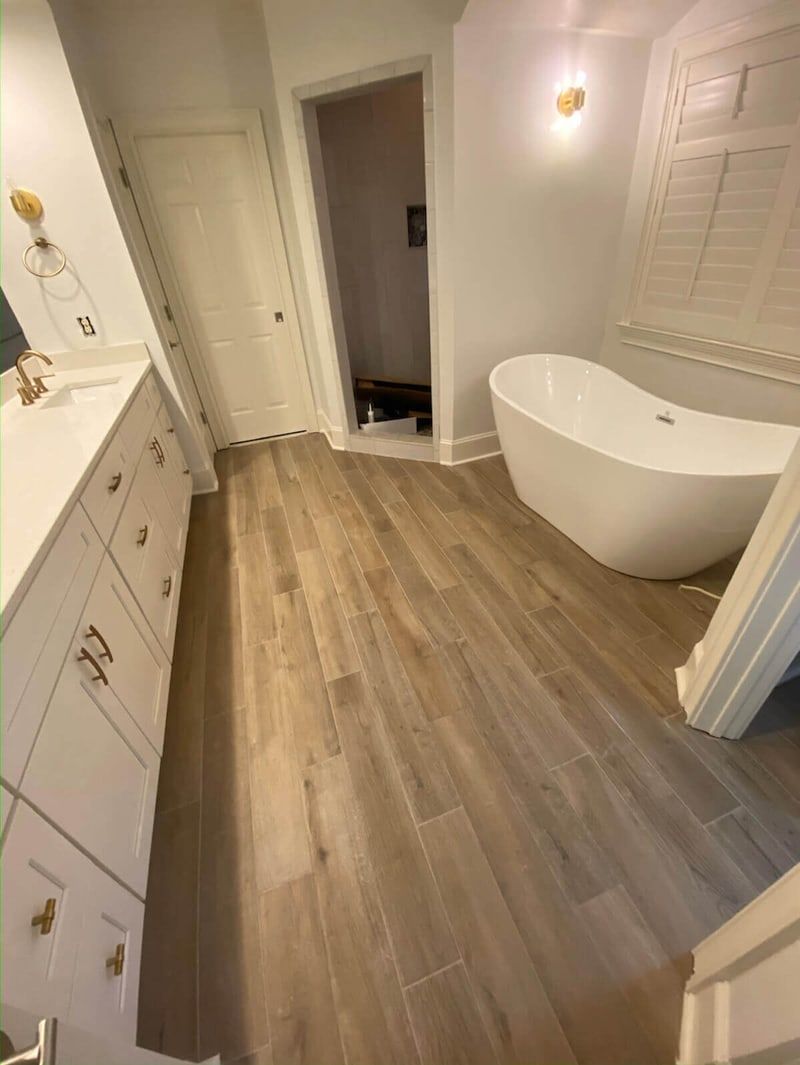Bathroom with white cabinets, tub, and light wood-look tile.
