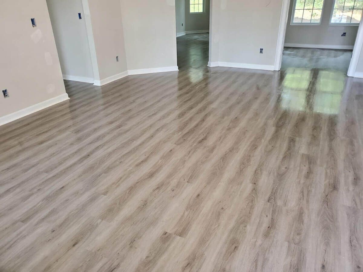 Light-toned wood-look flooring in a room with neutral walls and trim, reflecting light from a window.