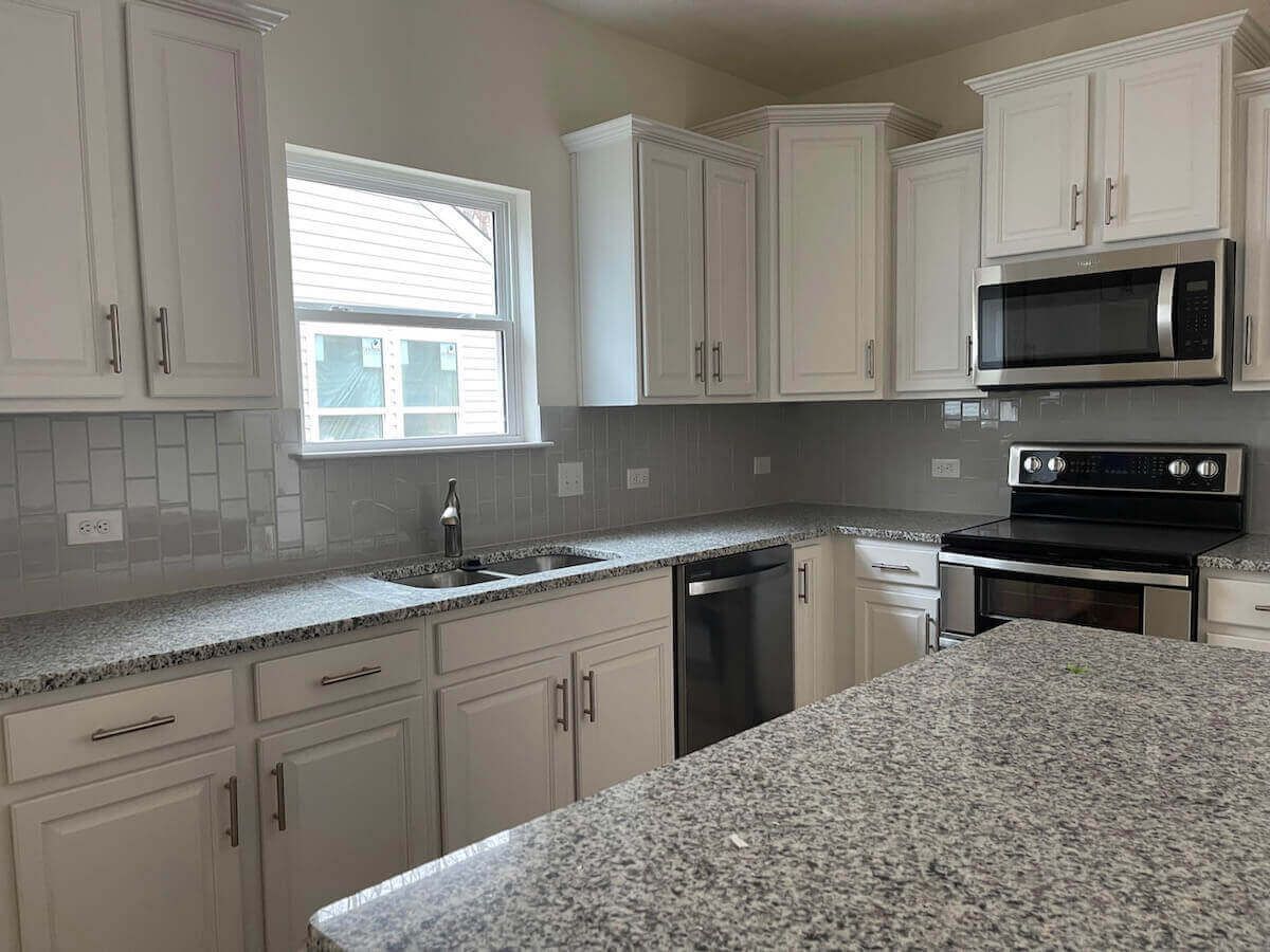 White kitchen with granite countertops, stainless steel appliances, and a window.