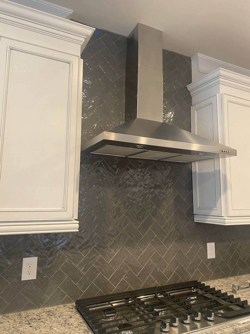 Kitchen with stainless steel range hood, gray backsplash, white cabinets, and gas cooktop.