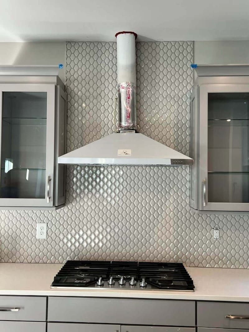 Kitchen with a range hood, stovetop, backsplash, and cabinets.