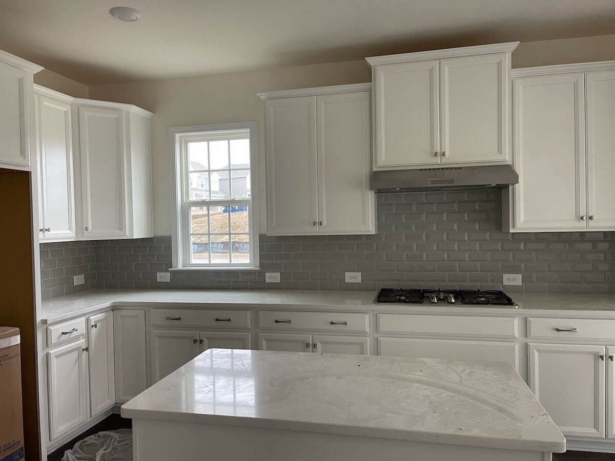 White kitchen cabinets with gray backsplash and countertop, window and island.