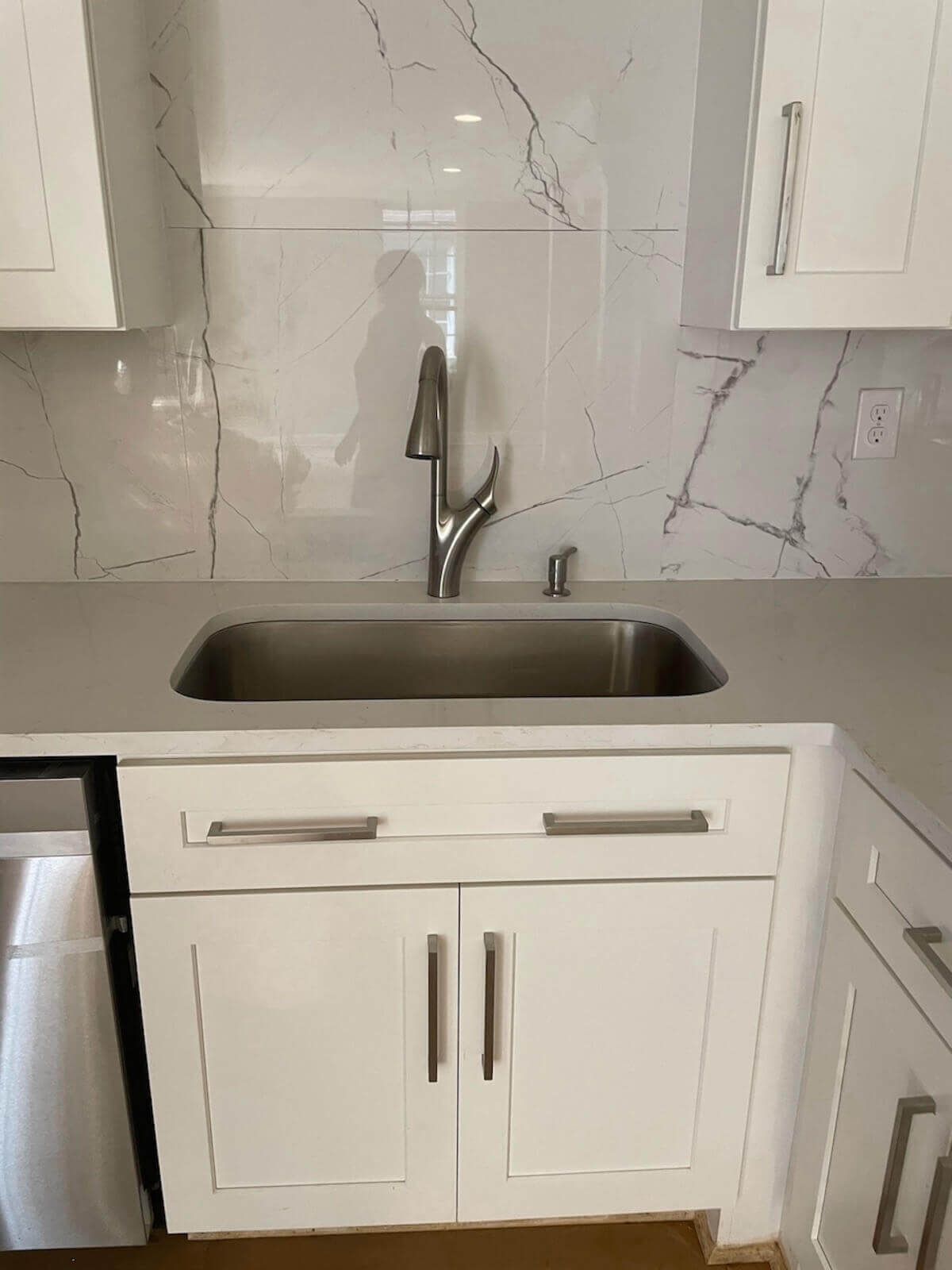 White kitchen sink and cabinets with silver faucet and marbled backsplash.