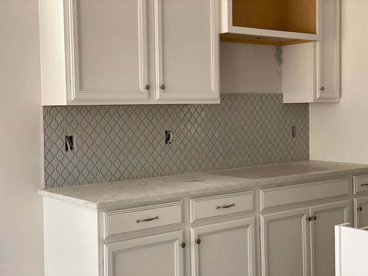 White kitchen cabinets with gray patterned backsplash and countertop.