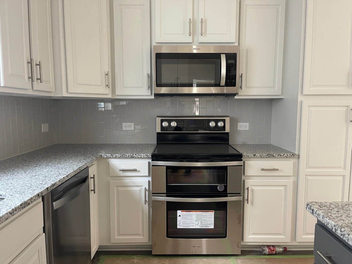 Kitchen with white cabinets, stainless steel appliances, gray granite countertops, and tile backsplash.