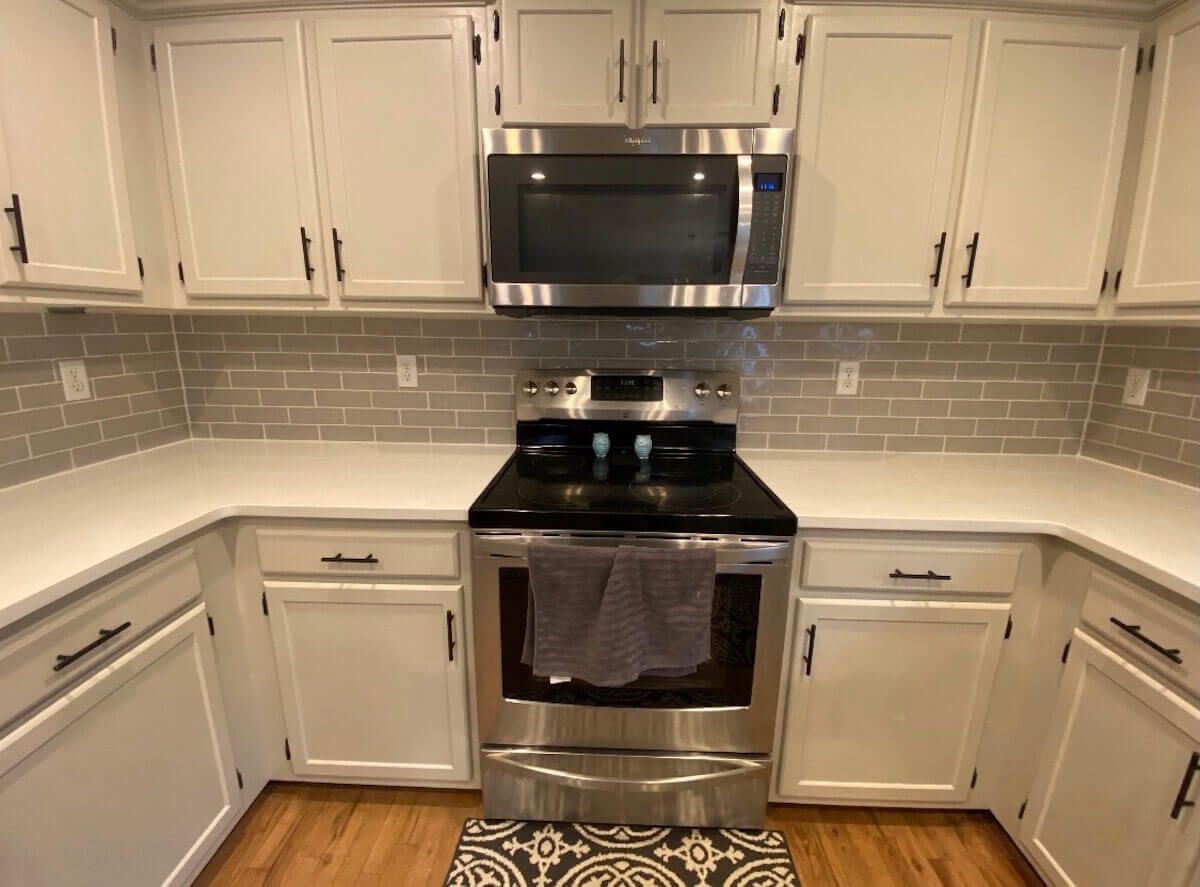 Kitchen with white cabinets, stainless steel appliances, and gray tile backsplash.