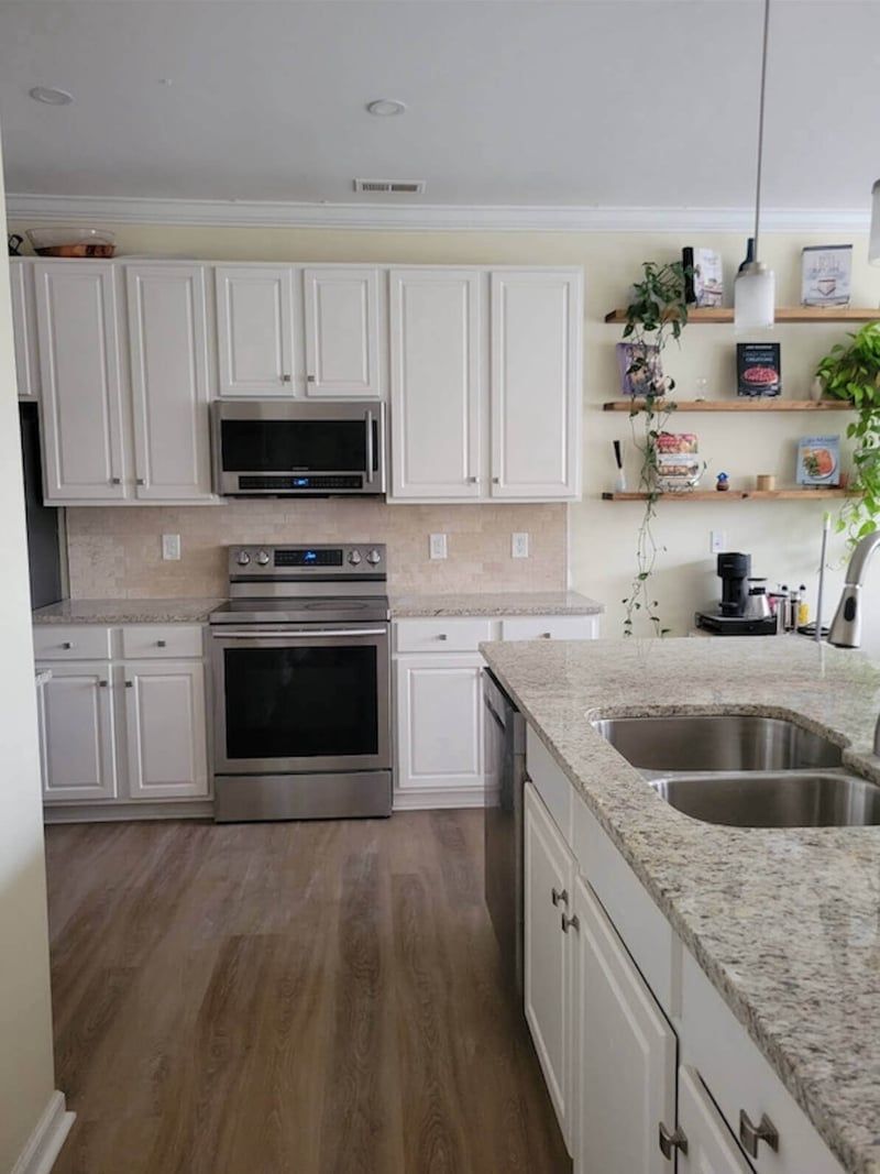 White kitchen with stainless steel appliances, granite countertops, and light wood flooring.