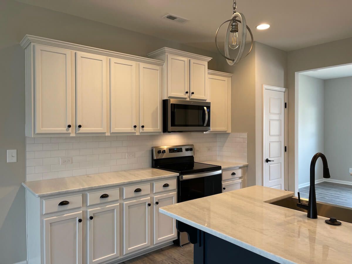 White kitchen cabinets with black hardware and a stainless steel microwave and stove.