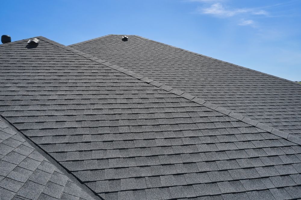 Gray asphalt shingle roof against a blue sky, vents visible.