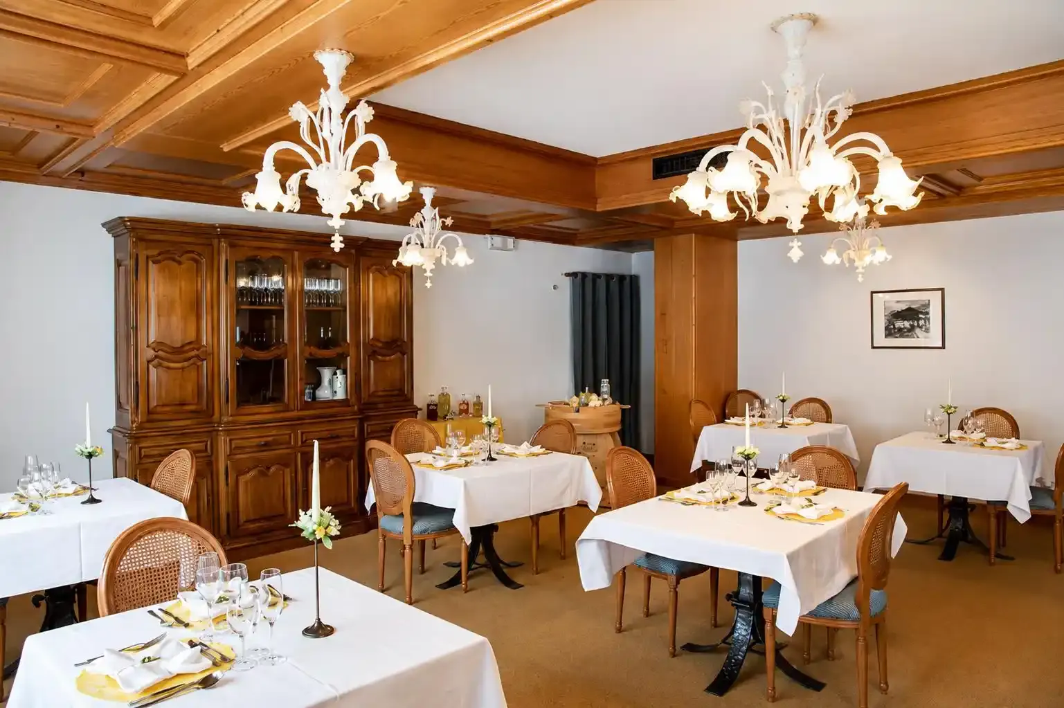 Elegante sala da pranzo di un ristorante con tavoli apparecchiati, lampadari bianchi e mobili in legno.