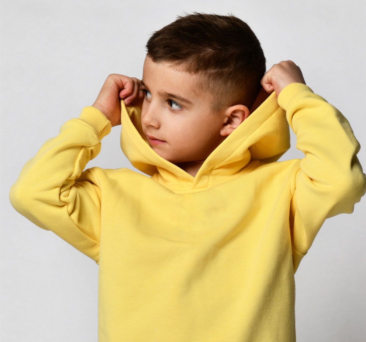 Boy in yellow hoodie pulling up the hood, looking to the side.