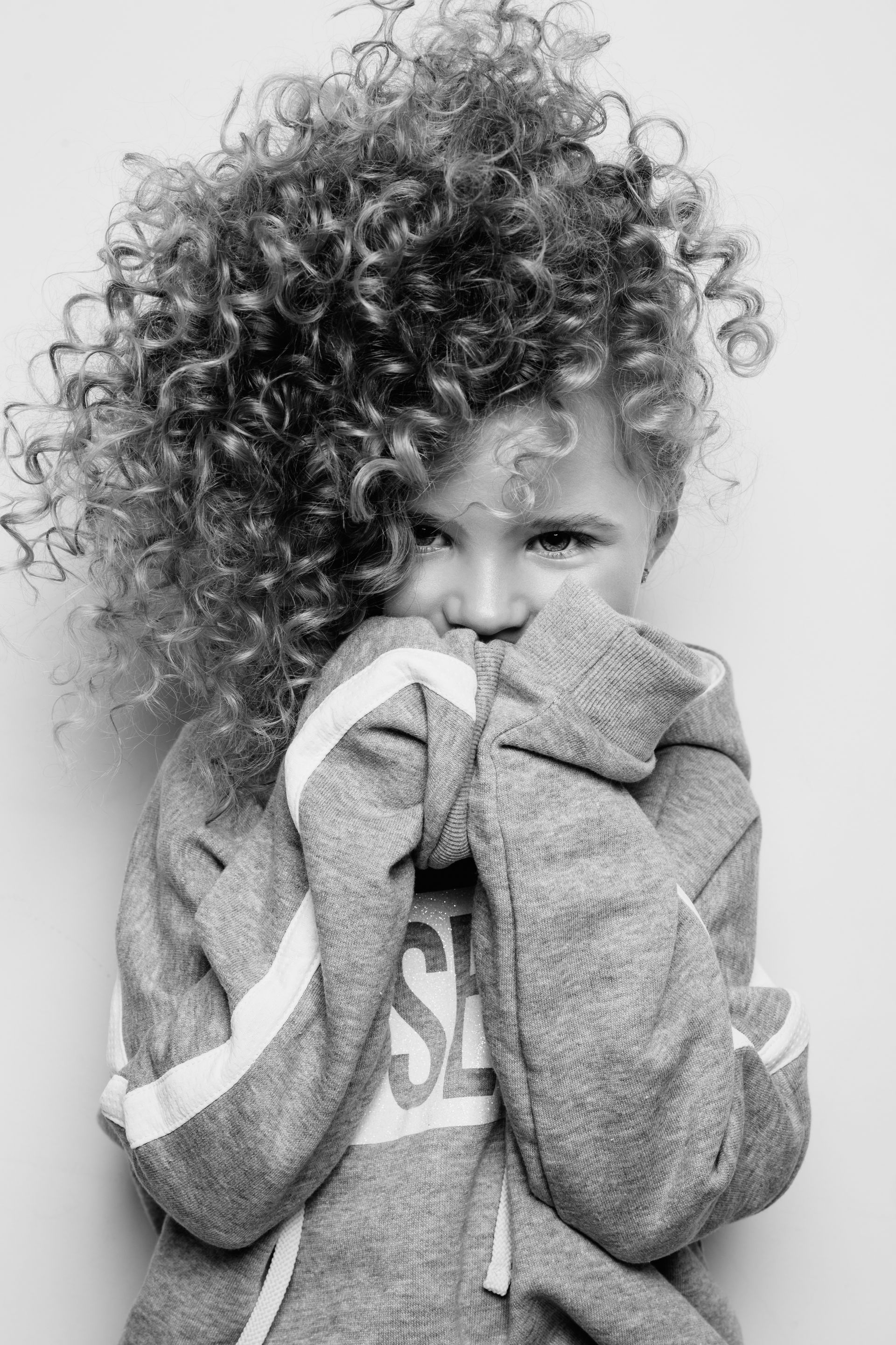 A black and white photo of a little girl with curly hair covering her face.