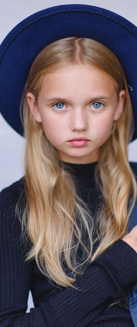 A young girl wearing a blue hat and a black sweater.