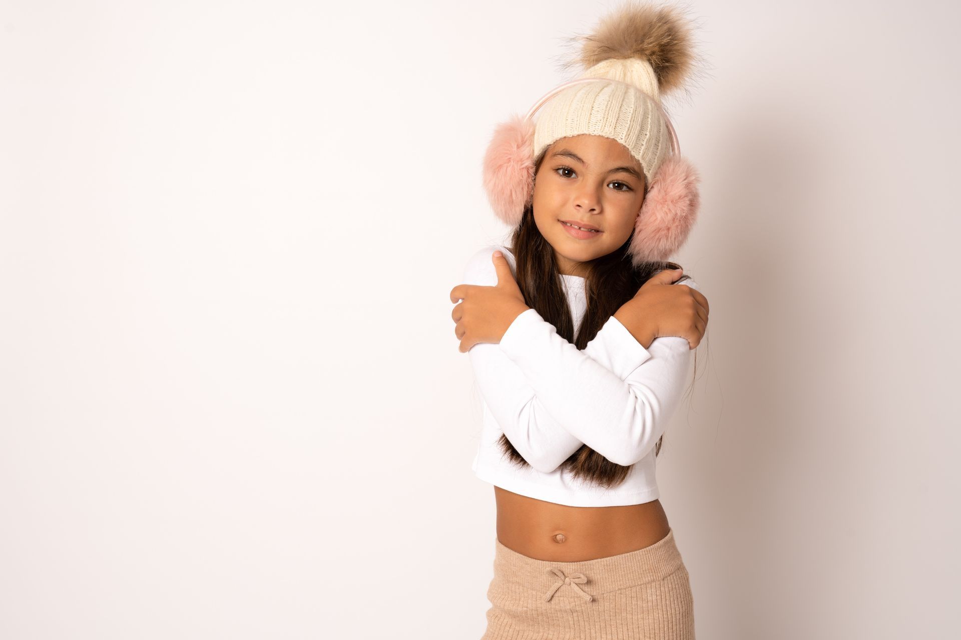 Boy wearing a gray beanie, white shirt, and blue sweater against a yellow wall.