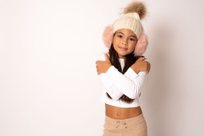 Boy wearing a gray beanie, white shirt, and blue sweater against a yellow wall.