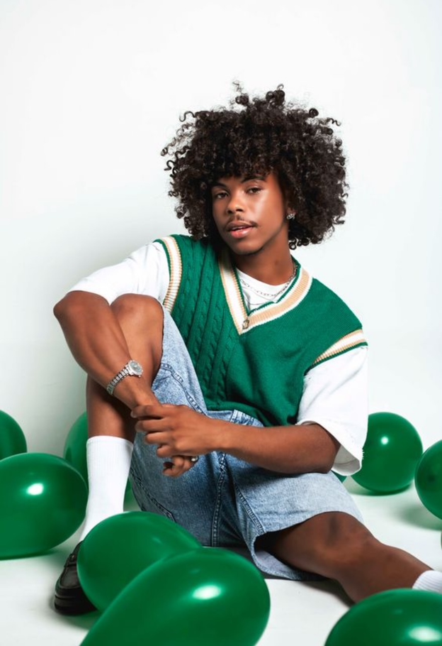 Girl with curly hair, pink shirt, smiling, pointing to the right against a yellow background.