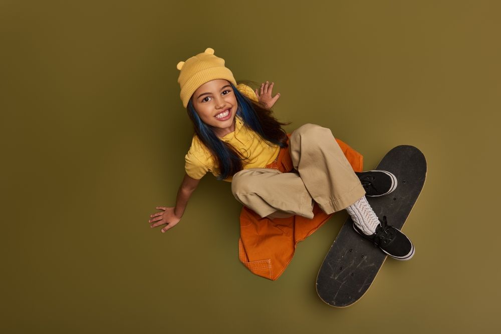 A young girl is sitting on a skateboard on a green background.