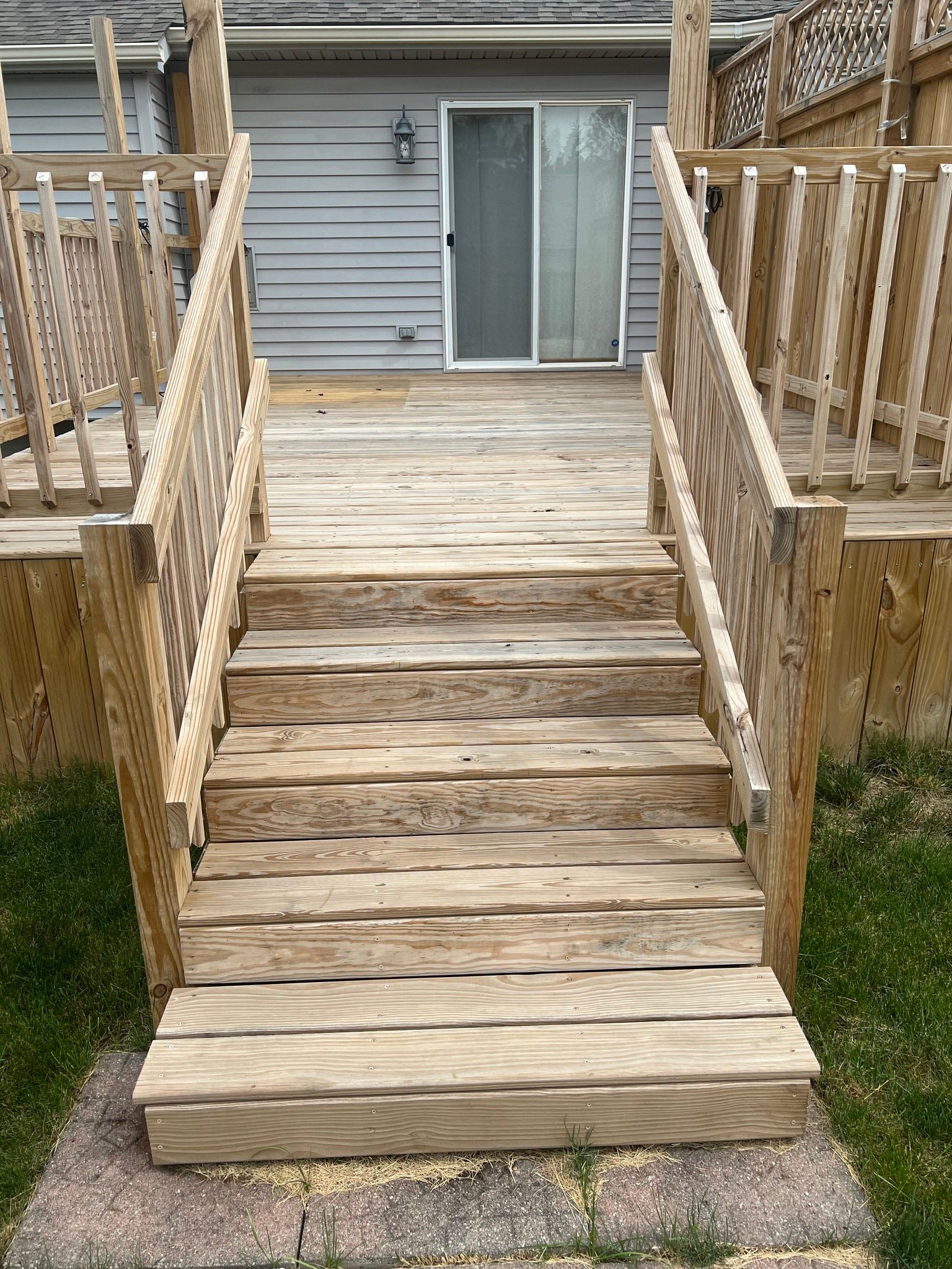 A wooden deck with stairs leading up to it and a sliding glass door.