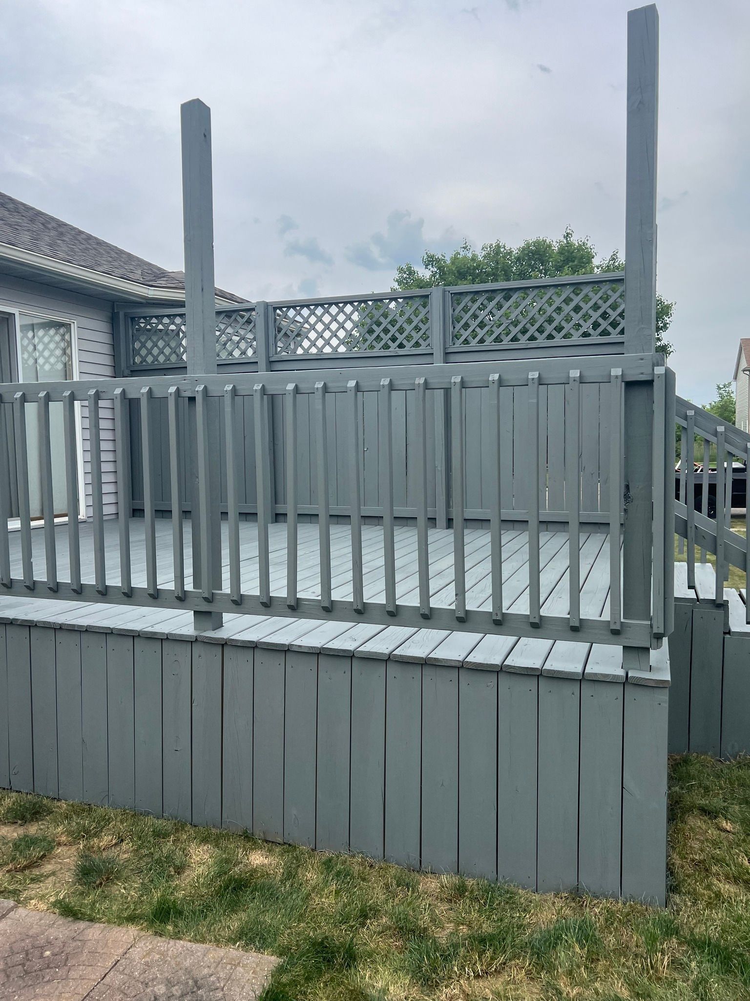 A gray deck with a fence around it and a house in the background.
