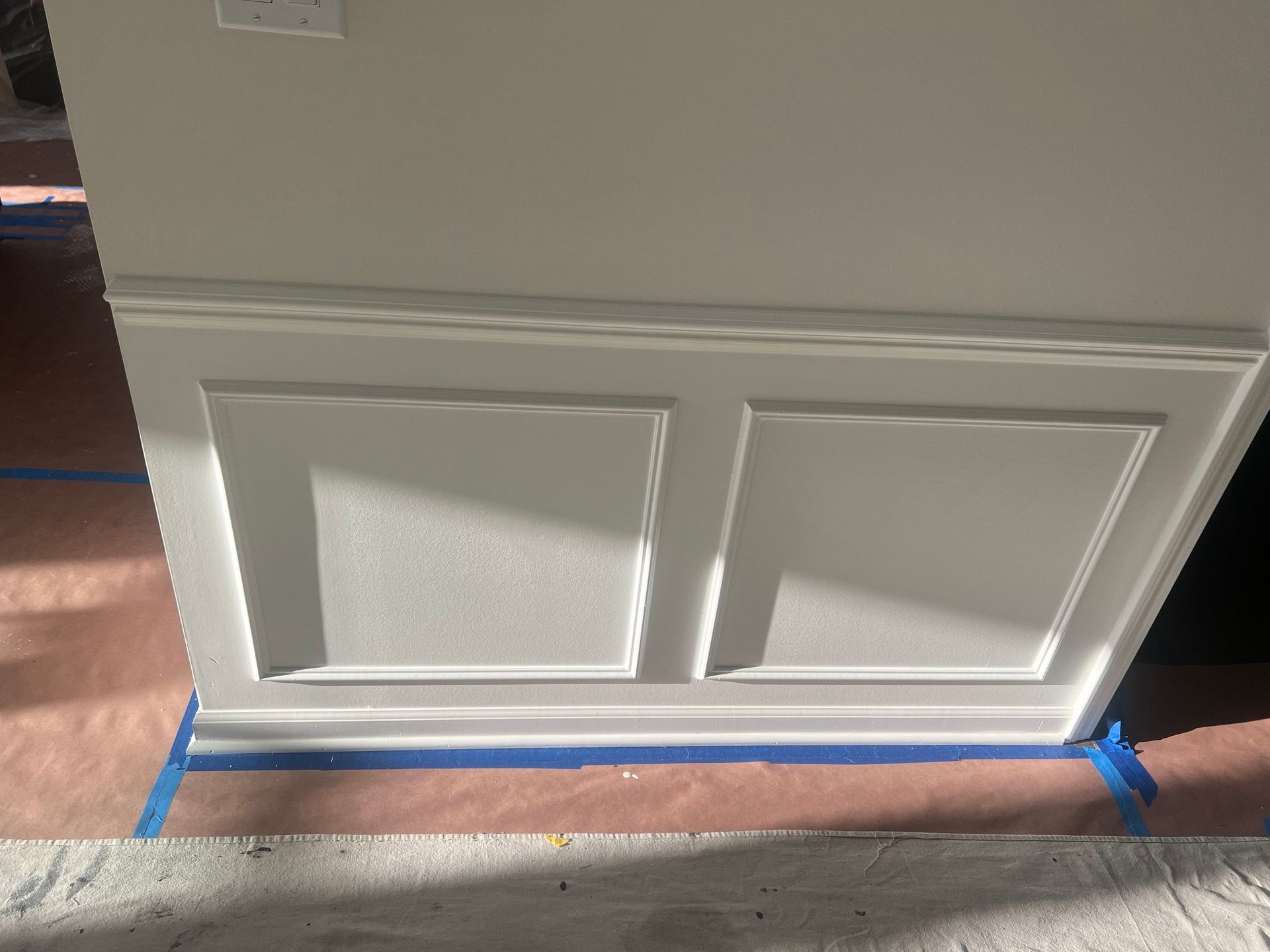 A white wall with blue tape on it is being painted.