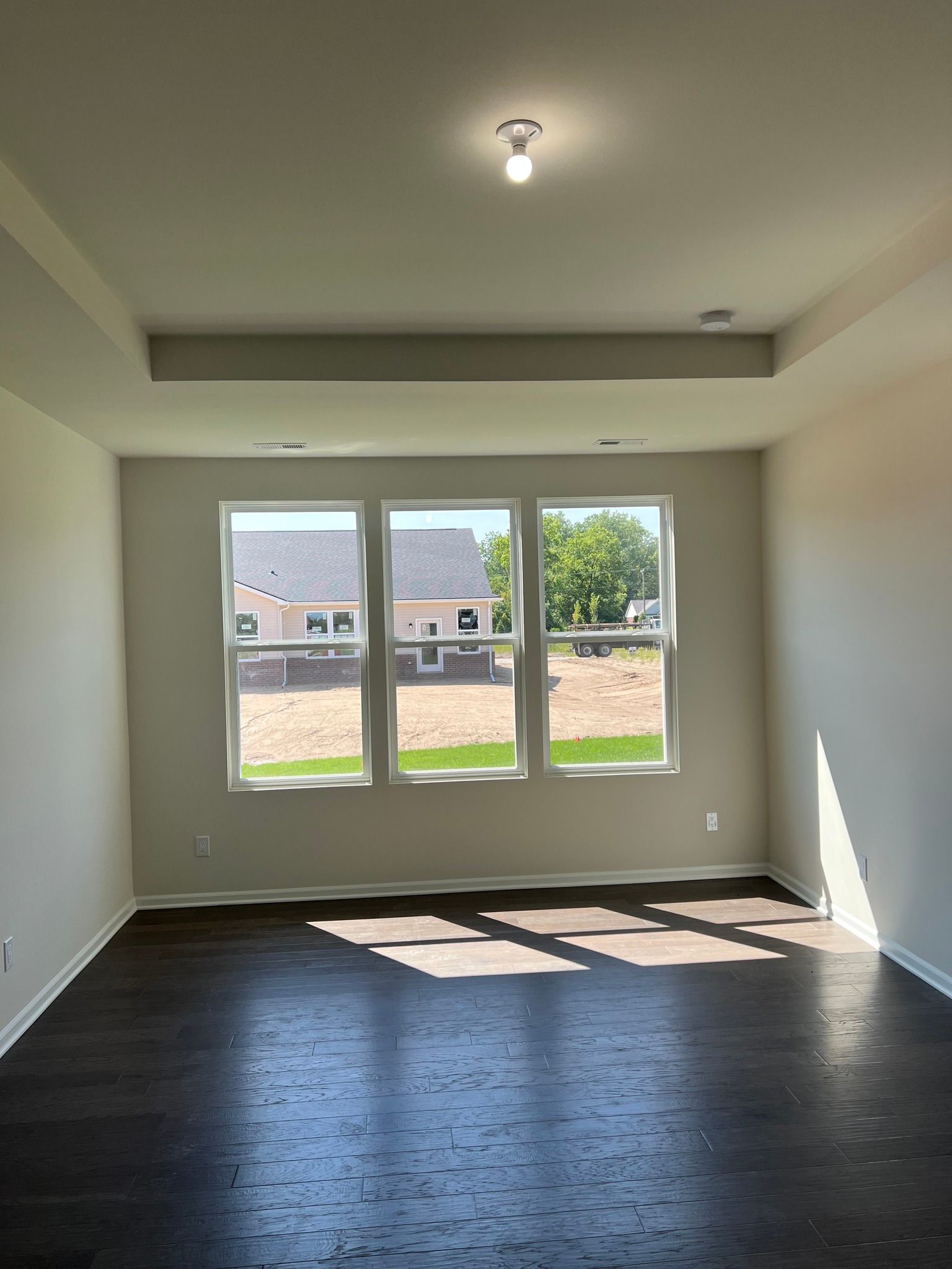An empty living room with hardwood floors and three windows.