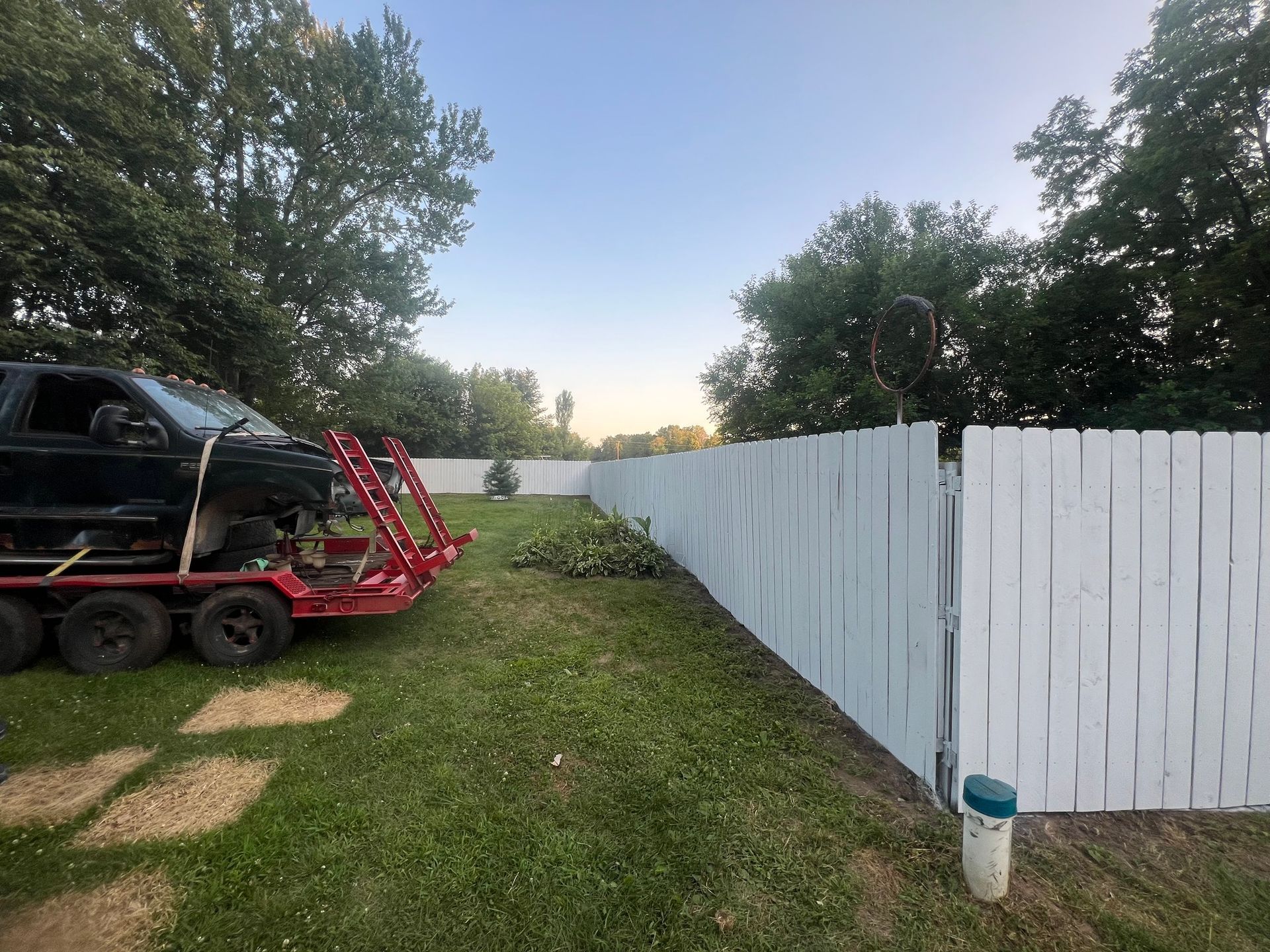 A black truck is on a trailer next to a white fence.
