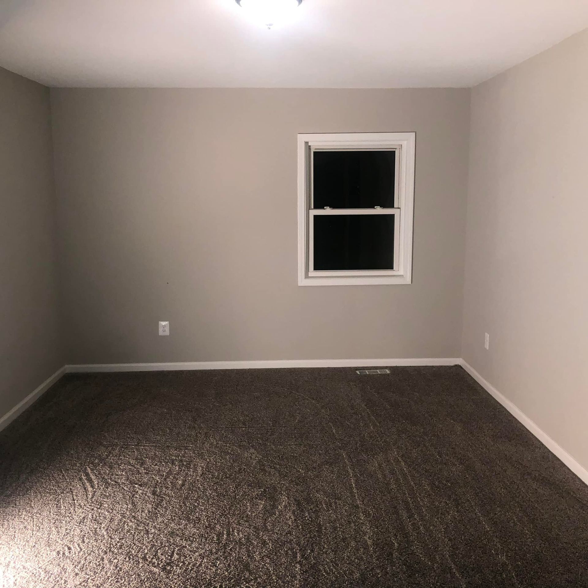 An empty room with a window and a carpeted floor.