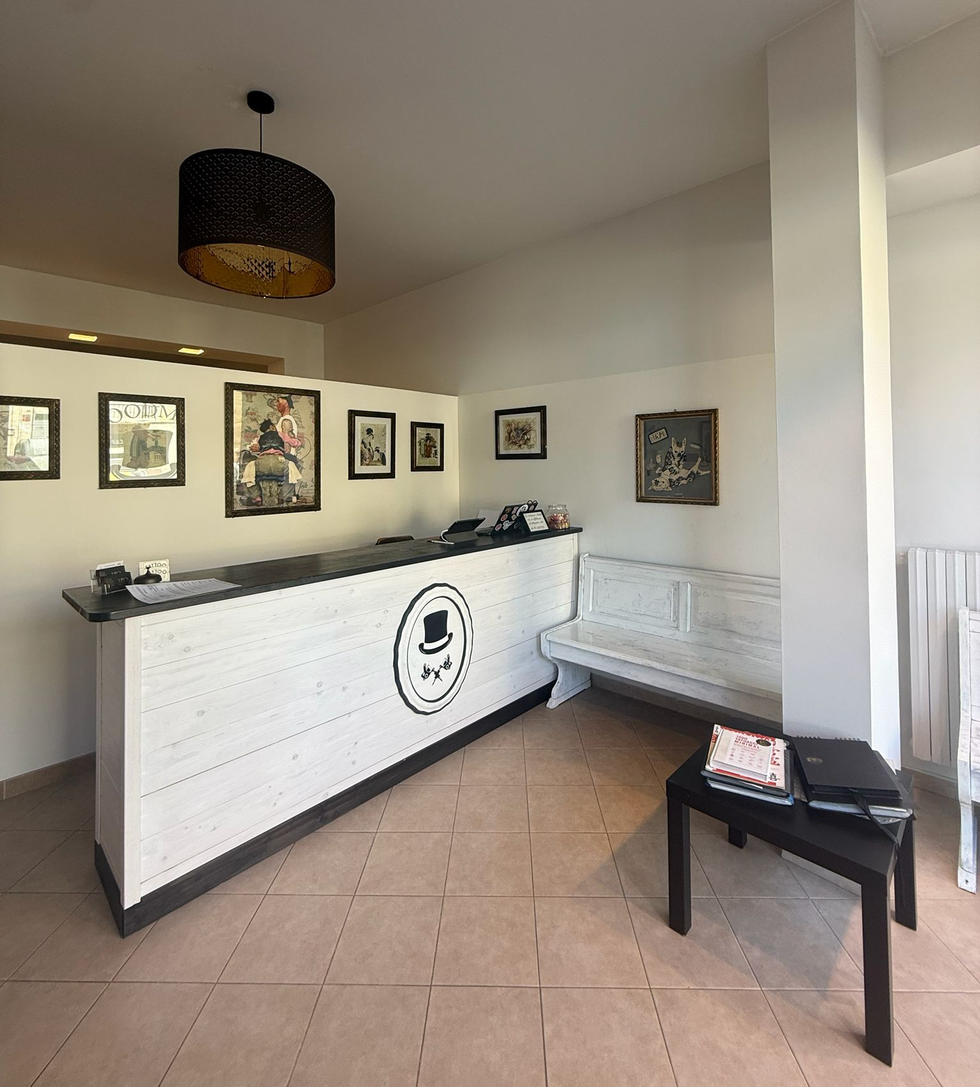 Banco reception in una luminosa sala d'attesa con quadri alle pareti, panca bianca e tavolino da caffè nero.
