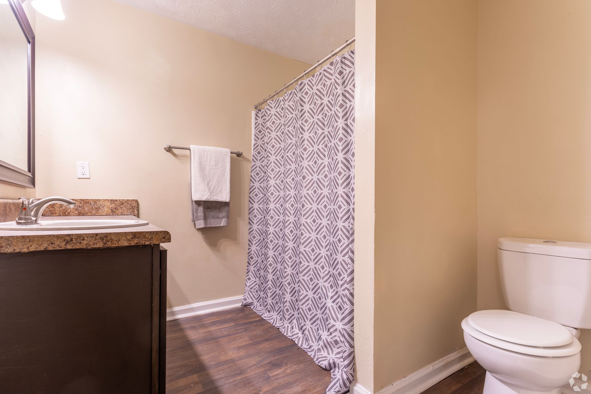 A bathroom with a dark wood vanity, a marble-look countertop, a patterned shower curtain, and a white toilet.