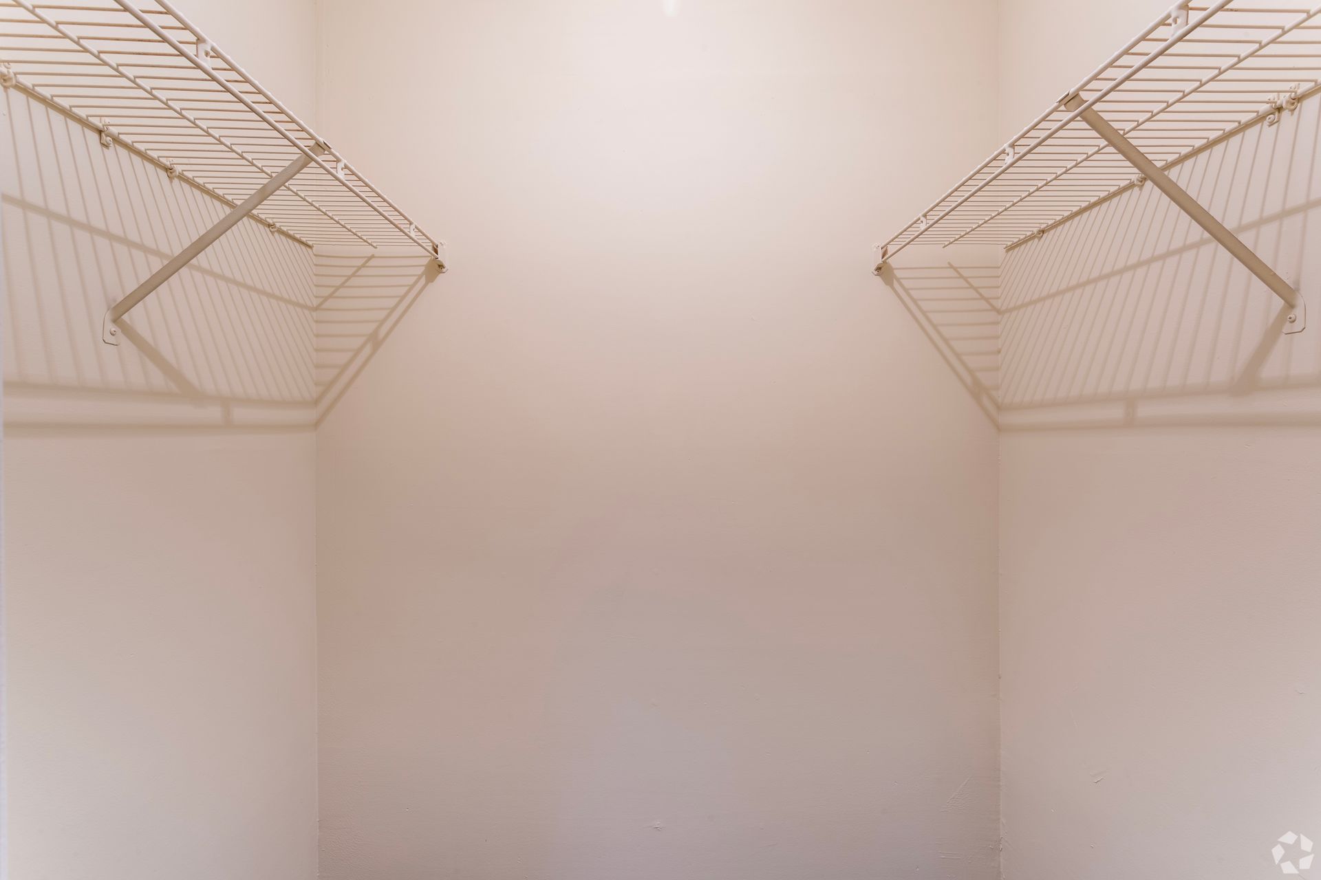 An empty walk-in closet with beige walls and white wire shelving units mounted on opposite walls.