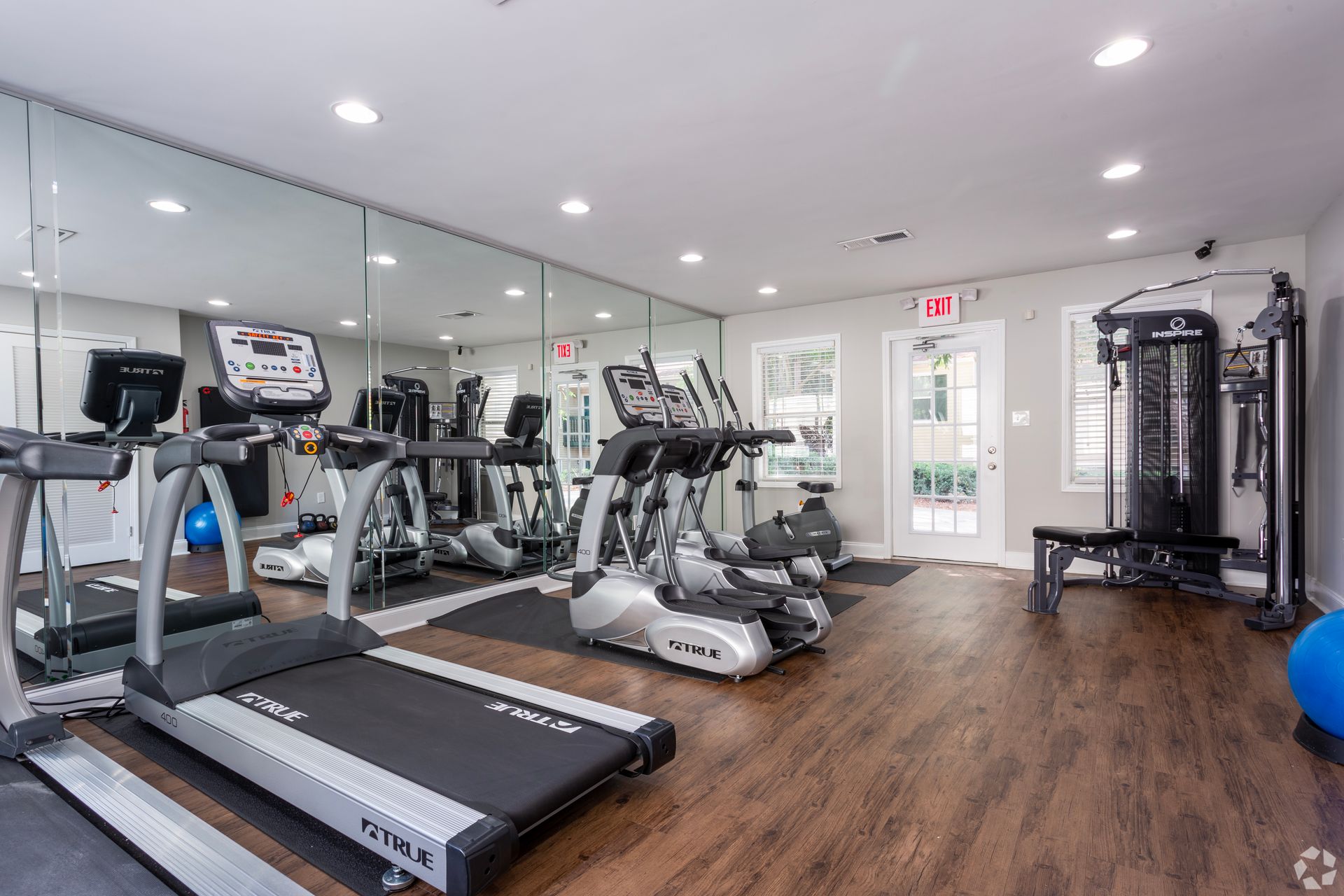 A gym interior with treadmills, a weight machine, mirrors on the wall, and hardwood flooring.