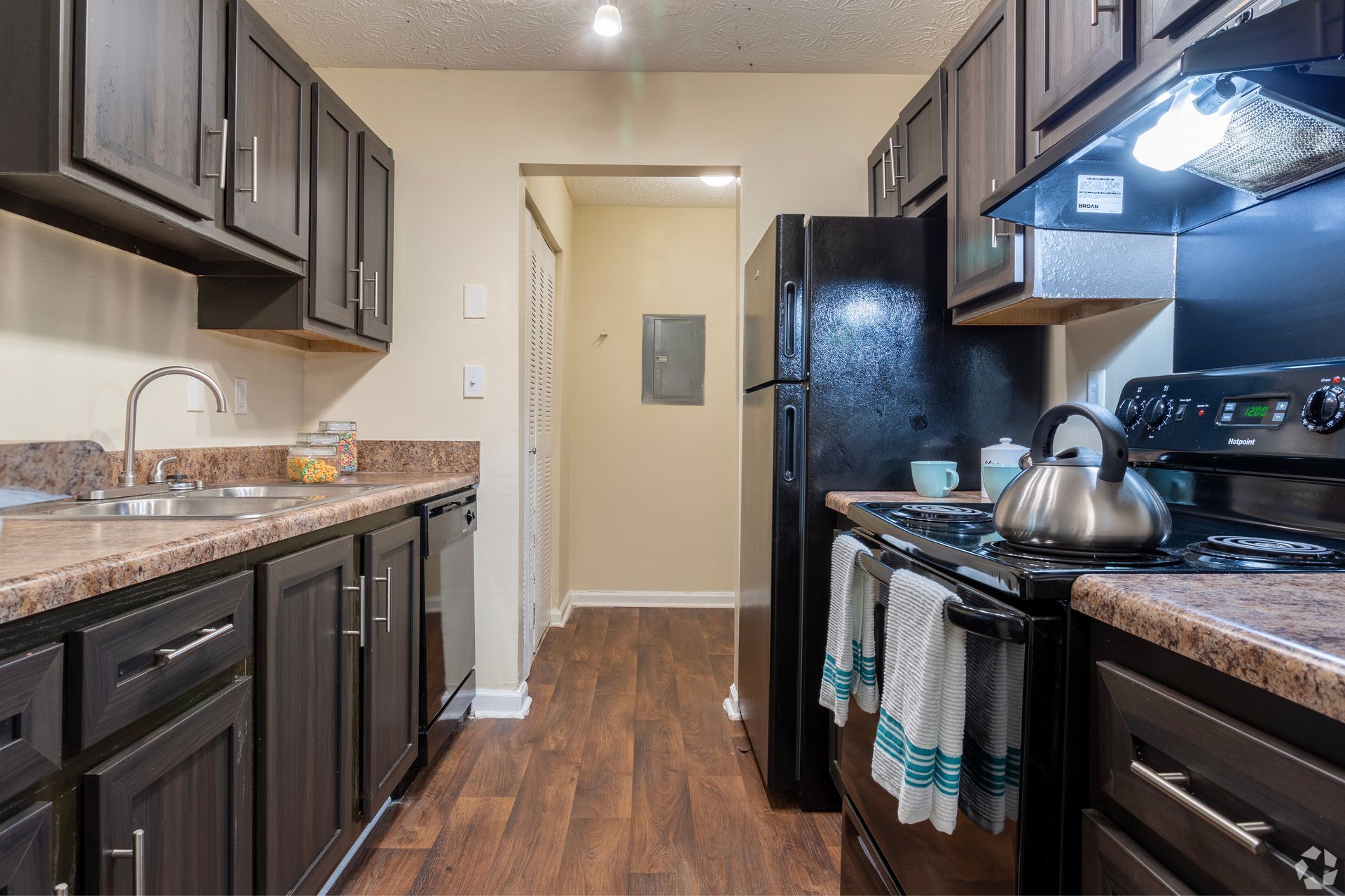 A kitchen with dark wood cabinets, black appliances, tan countertops, and wood-look flooring.