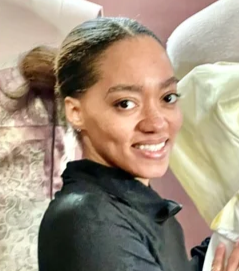 A person with dark hair pulled back in a ponytail smiling while wearing a black collared shirt.