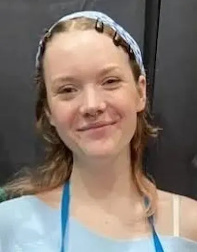 Smiling person in a light blue top and headband against a dark background