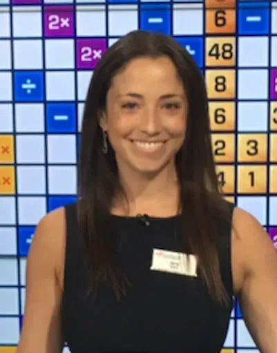 Smiling woman in a black dress standing before a colorful game board backdrop