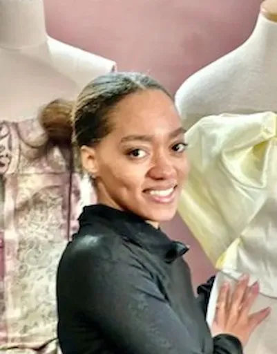 Smiling person in a black jacket posing indoors beside large decorative figures