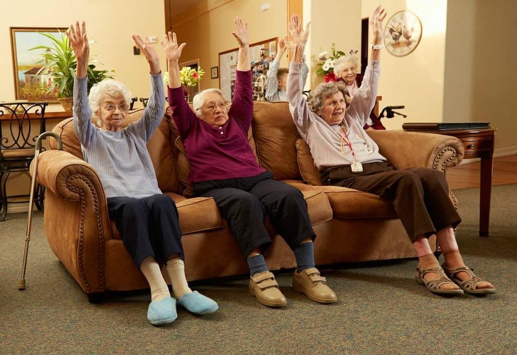 A woman is standing in front of a group of elderly people with their hands in the air.