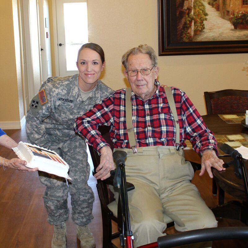 An elderly man is sitting on a couch with a nurse standing next to him.