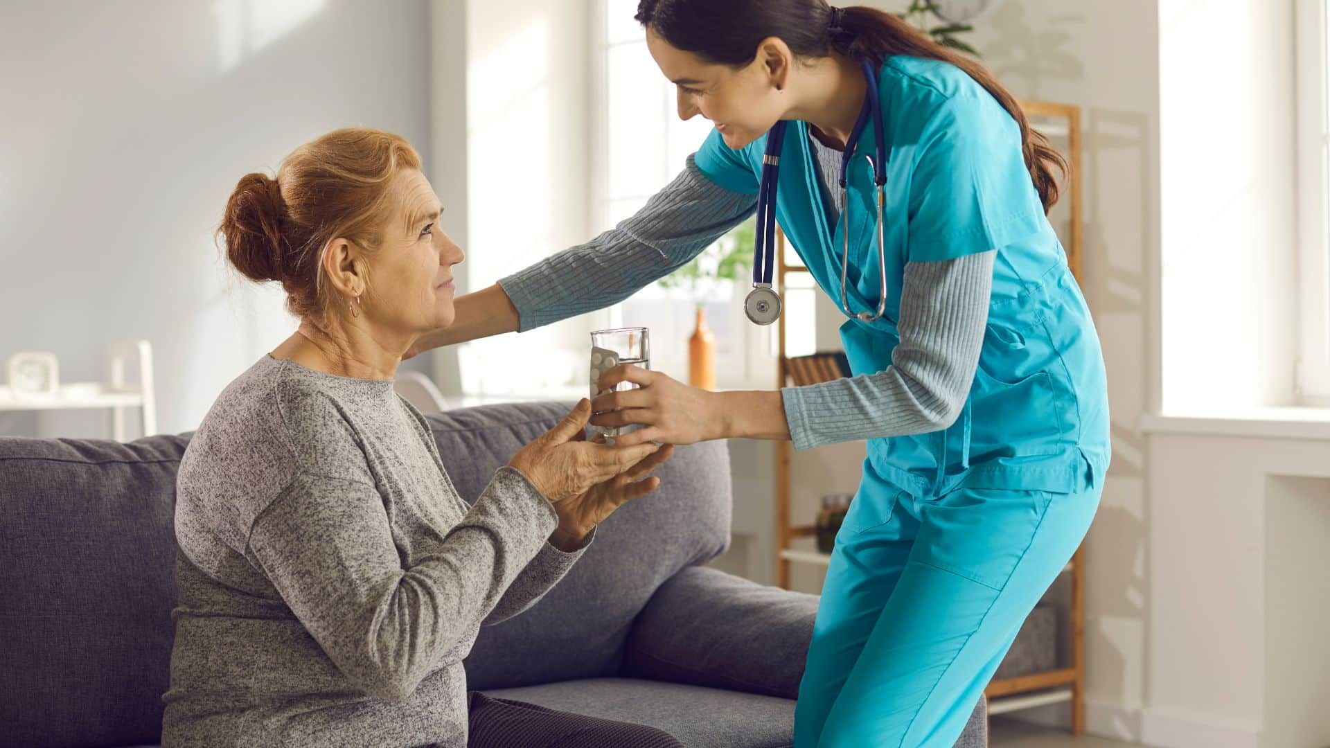 A nurse is giving an elderly woman a glass of water.