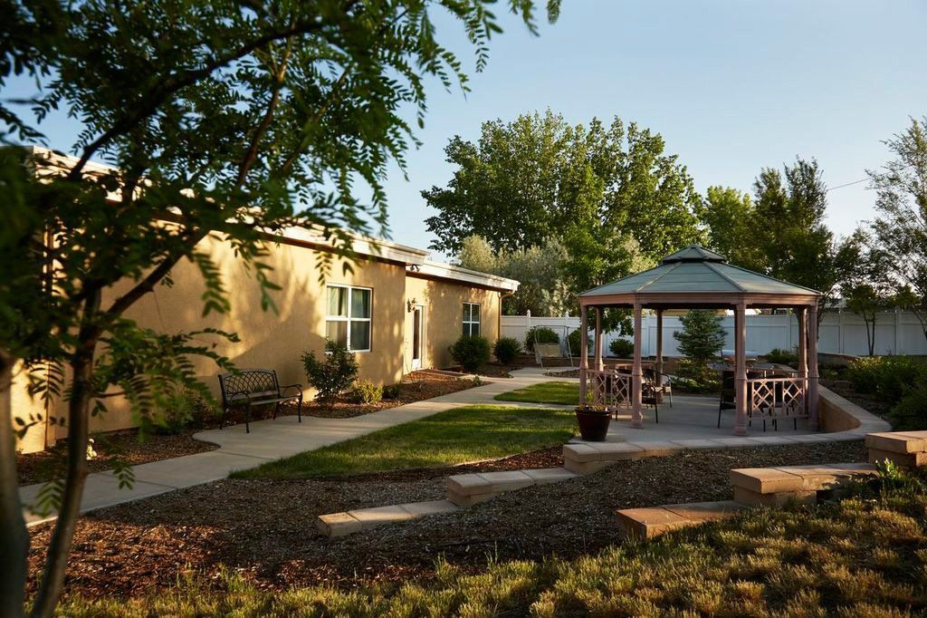 A gazebo is in the middle of a lush green yard in front of a house.